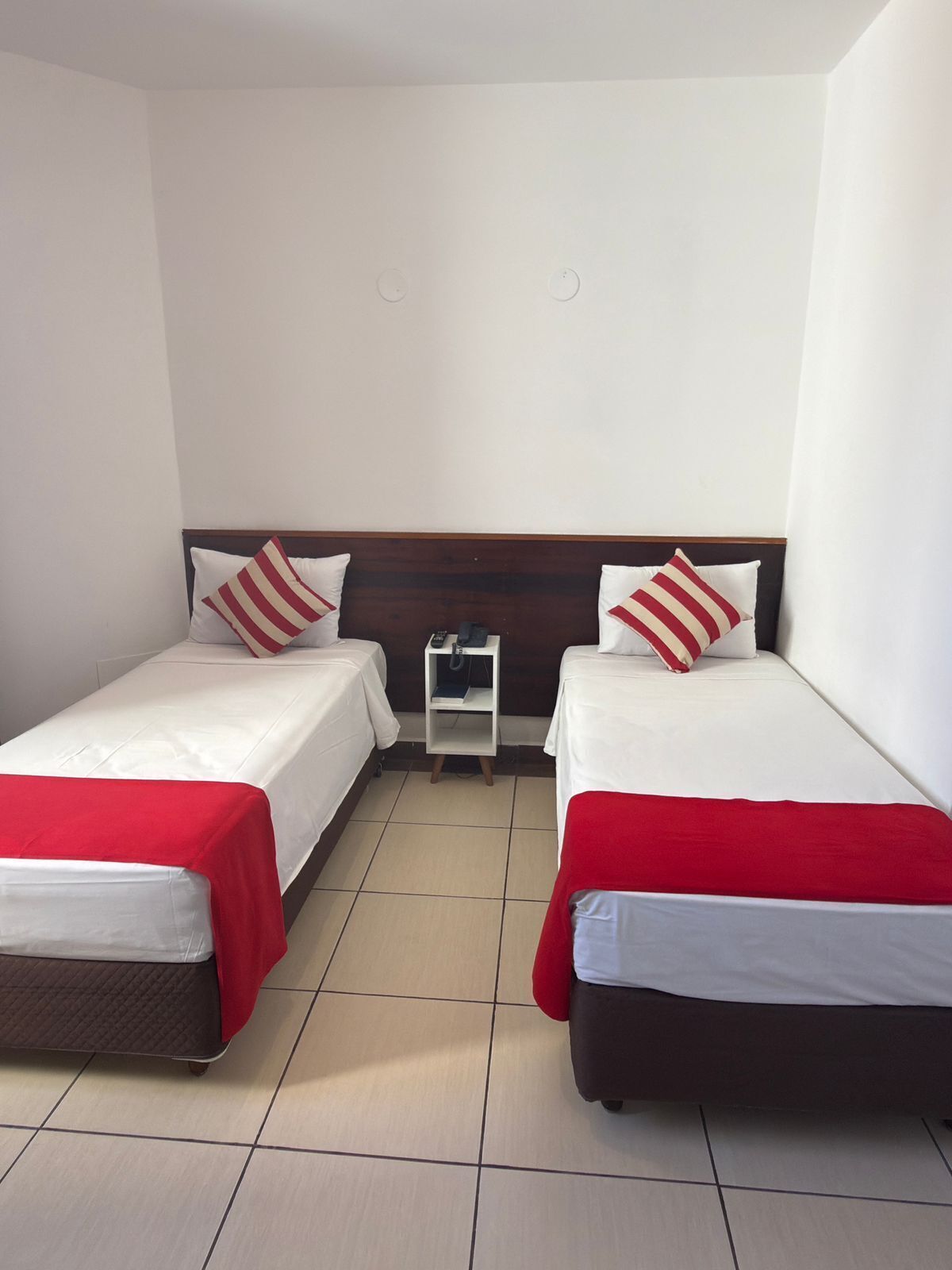 A hotel room with two beds, each with a red and white striped pillow, a small bedside table with a phone, and a red blanket on each bed.