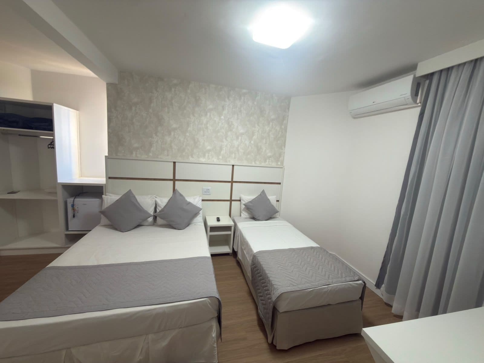 A hotel room with two beds, a wardrobe, a desk, and an air conditioning unit.