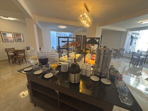 A buffet setup with various food items, a coffee station, and a decorative chandelier. - GRANCENTRO HOTEL (Mogi-Guacu)