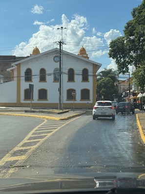 A street view with a white building with yellow trim, a stop sign, and cars on the road. - GRANCENTRO HOTEL (Mogi-Guacu)