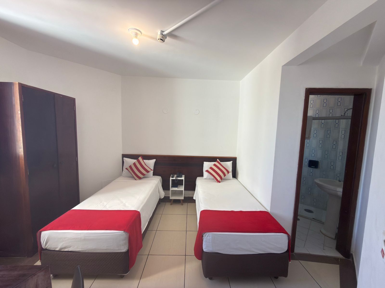 A room with two beds, a wardrobe, a small table, and a bathroom visible through an open door.