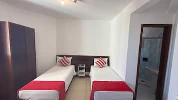 A room with two beds, a wardrobe, a small table, and a bathroom visible through an open door.