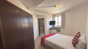 Een slaapkamer met een bed, televisie, kast en een badkamer die door een open deur zichtbaar is.