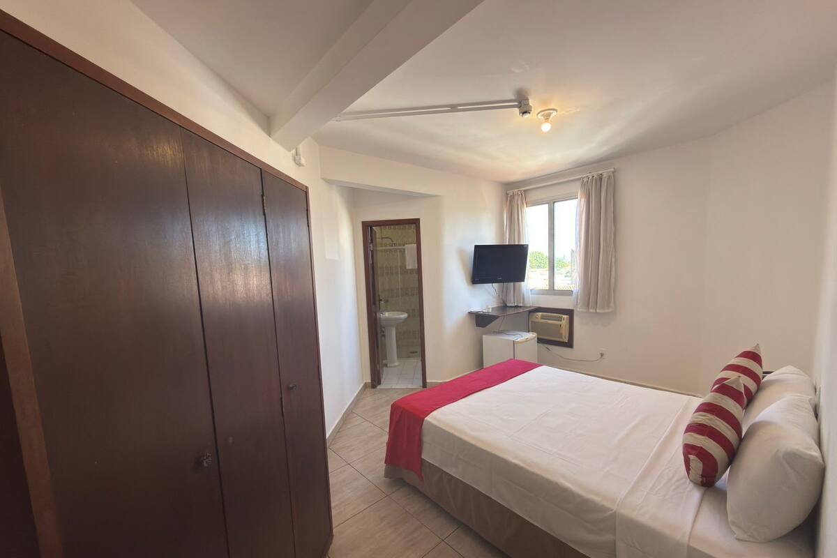 A bedroom with a bed, a TV, a wardrobe, and a bathroom visible through an open door.