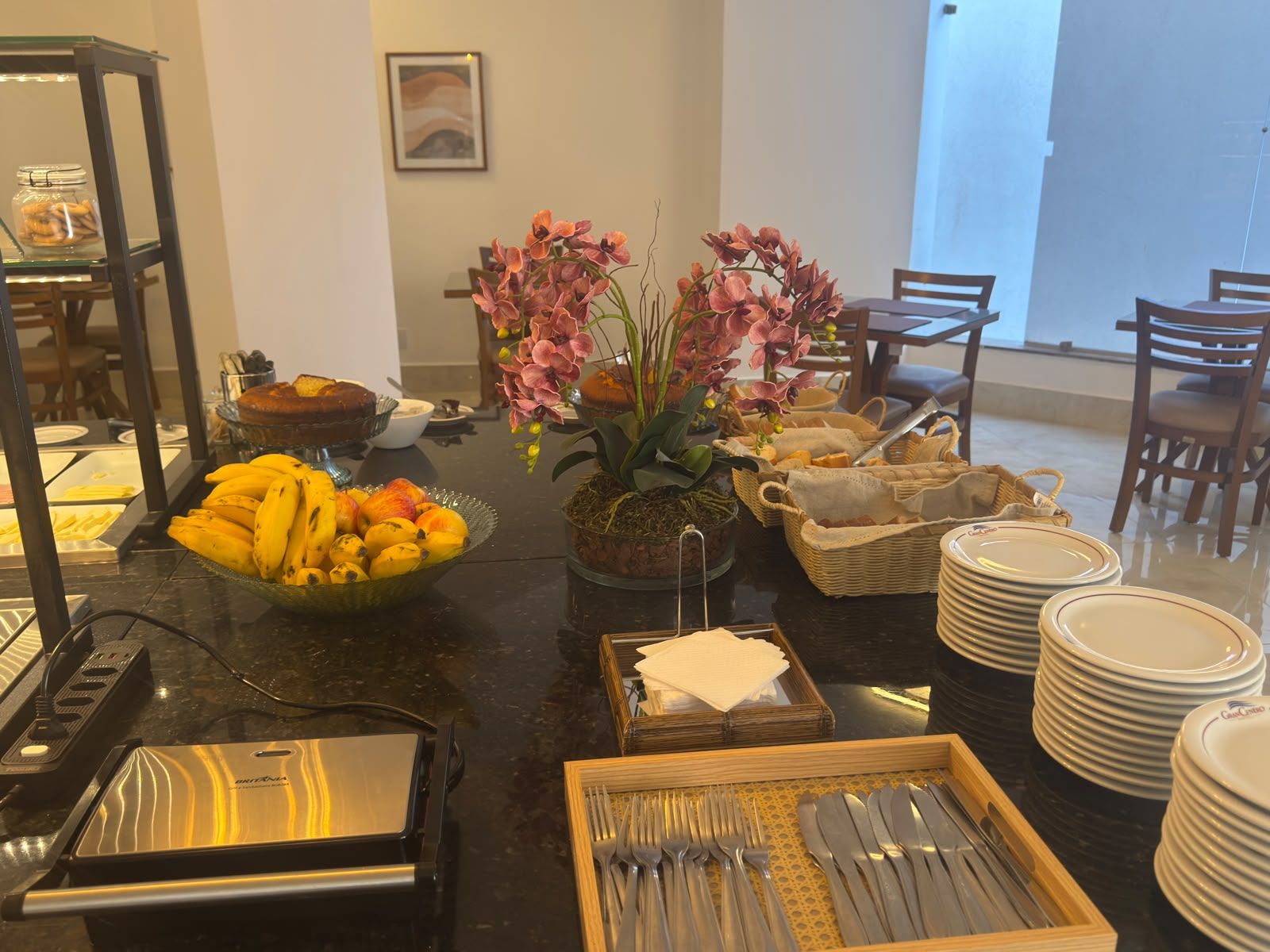 A buffet setup with various food items, a fruit bowl, a flower arrangement, and stacked plates.