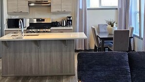 Une cuisine moderne dotée d’un îlot central, un coin repas avec une table et des chaises, et un salon avec un canapé et un coussin décoratif.