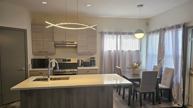 Une cuisine moderne dotée d’un îlot central, d’appareils électroménagers en acier inoxydable et d’un coin repas avec des chaises et une table.