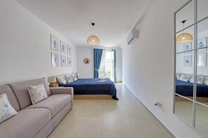 A bedroom with a bed, a sofa, a mirror, and framed artwork on the wall. - Gozo Getaway - Large Pool Apartment, 10 mins to Xagħra Square (Ix-Xagħra)