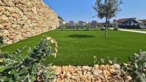 Un muro in pietra, un prato curato e una fila di lettini da sole.