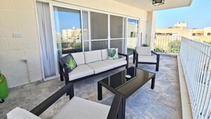 Un balcone con un divano, poltrone e un tavolino in vetro.