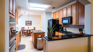 A kitchen with wooden cabinets, a black refrigerator, a stove, and a dining area with a table and chairs. - Beautiful 3-bedroom house in The Woodlands (Spring)