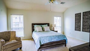 A bedroom with a bed, two windows, a chair, a nightstand, and wall art. - Beautiful 3-bedroom house in The Woodlands (Spring)