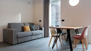 A modern living room with a grey sofa, a wooden dining table, and two chairs. - Apartment 3 Casa Bepa • In the heart of Bormio, ideal for skiing and relaxation (Bormio)