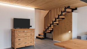 A modern interior with a wooden staircase, a flat-screen TV on a wooden dresser, and a dining table. - Apartment 3 Casa Bepa • In the heart of Bormio, ideal for skiing and relaxation (Bormio)