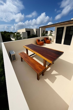 Eine Dachterrasse mit Holztisch und -bänken, einer Klimaanlage und orangefarbenen Stühlen.