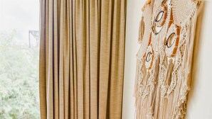 A room with a bed, a macrame wall hanging, and a view of greenery outside. - Welcome to your private oasis in the heart of Tulum! (Tulum)