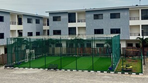 Un edificio a più piani con un'area sportiva recintata, che include una porta da calcio e una panchina.