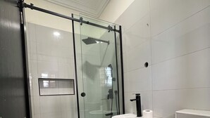 Un bagno moderno con doccia vetrata, lavandino bianco e piano di appoggio nero.