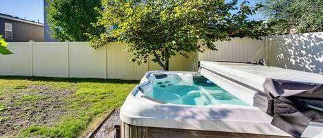 A hot tub in a backyard with a wooden deck, a tree, and a white fence.