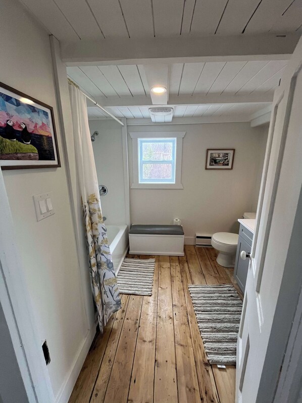 A bathroom with a wooden floor, a window, a toilet, and a bathtub.