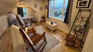 A cozy attic room with a bed, a rocking chair, a small table, a quilted chair, and a window with a view. - Wild Cove Retreat & Nook (Twillingate)