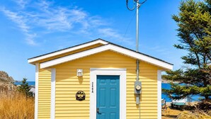 A small yellow building with a blue door, a mailbox, and a utility box. - Wild Cove Retreat & Nook (Twillingate)