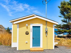Un petit bâtiment jaune avec une porte bleue, une boîte aux lettres et un coffret de raccordement.