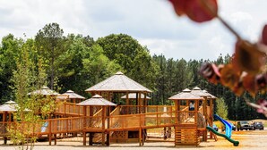 Un'area giochi con diverse strutture in legno, tra cui scivoli e zone dedicate all'arrampicata, immersa nel verde.