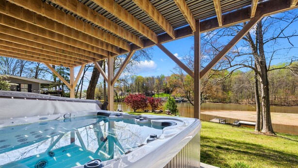 Una vasca idromassaggio sotto un gazebo in legno, con vista su un lago e alberi.