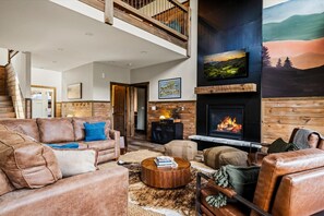 Ein geräumiges Wohnzimmer mit Kamin, Ledersofas, einem Couchtisch und einem großen, an der Wand befestigten Fernseher.