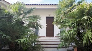 A building with a brown door, steps leading up to it, and surrounding greenery.