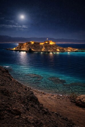 Una fortificación costera de noche con vistas despejadas al mar circundante y un cielo estrellado.