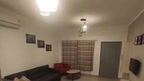 En stue med sofa, et rundt bord, et fjernsyn og en borddug med mønster.