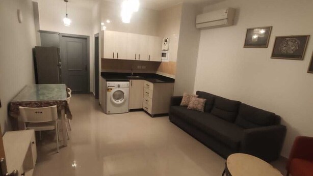 En kompakt opholdsstue med tekøkken, sofa, spisebord og et lille rundt bord.