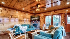 Interior acogedor de una cabaña con paredes de madera, una chimenea y un ventilador de techo.