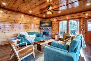 A cozy cabin interior with wooden walls, a fireplace, and a ceiling fan. - Sleeps 40 | 12BR, Indoor Pool, 2 Hot Tubs (Pigeon Forge)