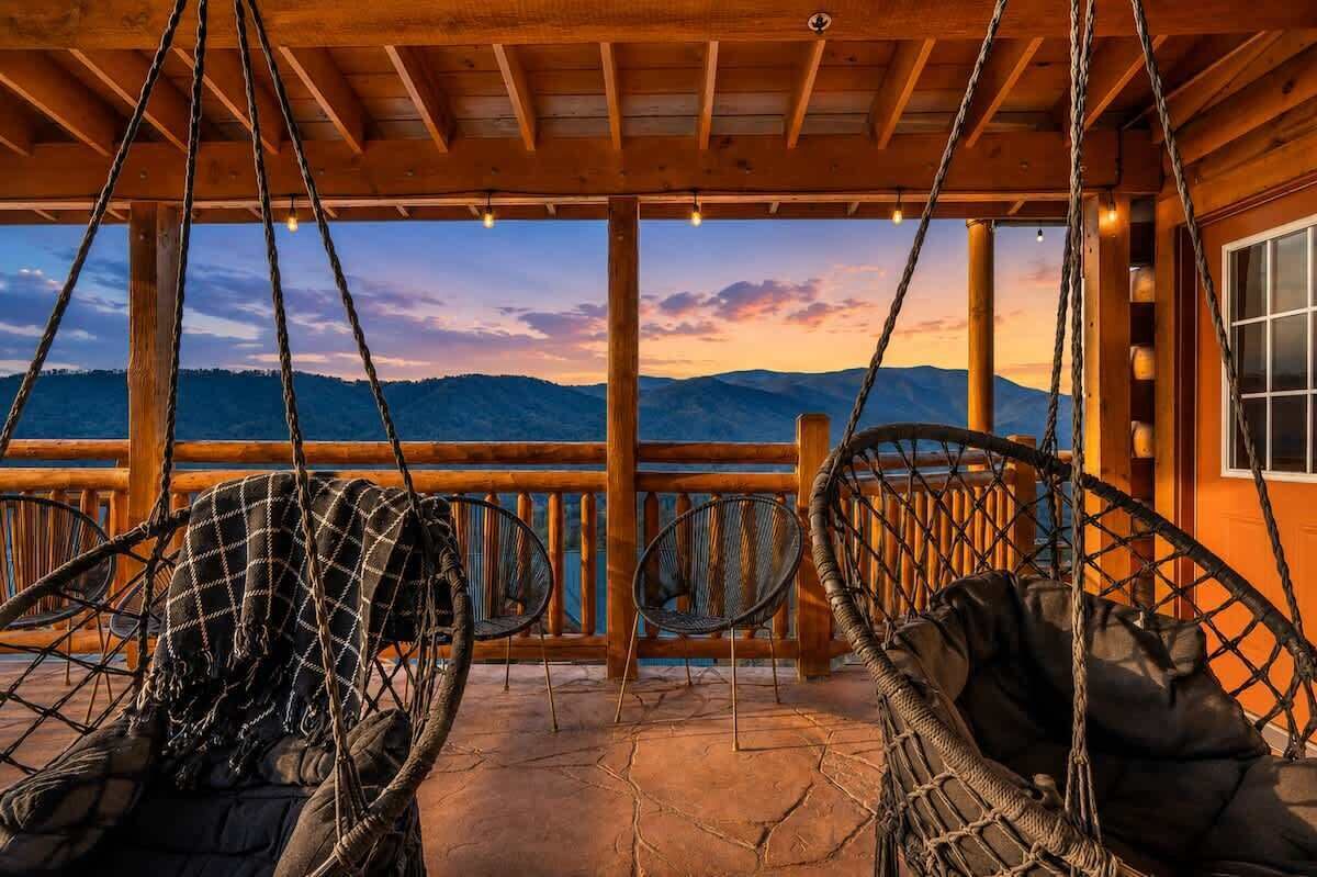 A wooden deck with a view of mountains, two wicker chairs, and a wooden railing.