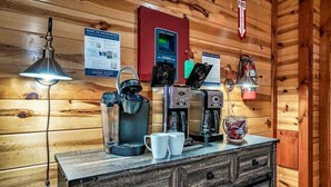 Interior de una cabaña de madera con una estación de café que incluye una cafetera, un hervidor y tazas.
