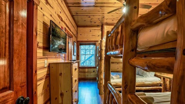 Interior de una cabaña de madera con literas, un televisor y una ventana con vistas a  árboles.