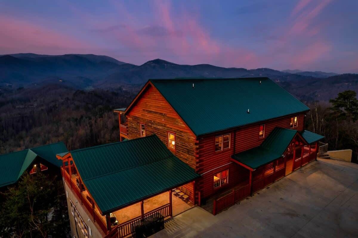 A log cabin with a green roof and a porch, surrounded by a mountainous landscape.