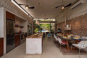 A modern kitchen with a central island, dining area with chairs, and a stone wall. - Beautiful modern house in Santiago (Mérida)