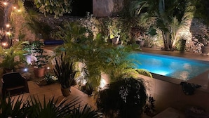 Ein Pool, umgeben von tropischen Pflanzen und Steinmauern, mit stimmungsvoller Beleuchtung.