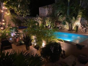 Ein Pool, umgeben von tropischen Pflanzen und Steinmauern, mit stimmungsvoller Beleuchtung.