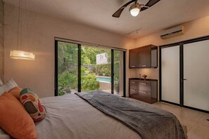 A bedroom with a bed, a ceiling fan, a nightstand, a window, and a view of a pool and greenery. - Beautiful modern house in Santiago (Mérida)