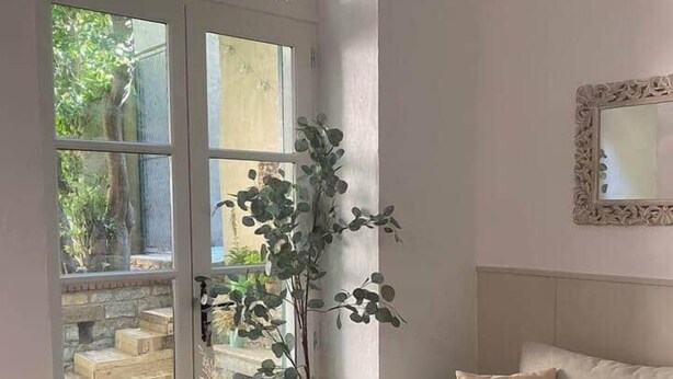 A room with a white couch, a wooden coffee table, a potted plant, and a window with a view of greenery. - Apartment with Private Garden Oasis in Central Carcassonne (Carcassonne)