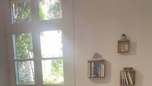 A room with a white armchair, a wooden floor, a glass door with a view, and a wall with bookshelves. - Apartment with Private Garden Oasis in Central Carcassonne (Carcassonne)