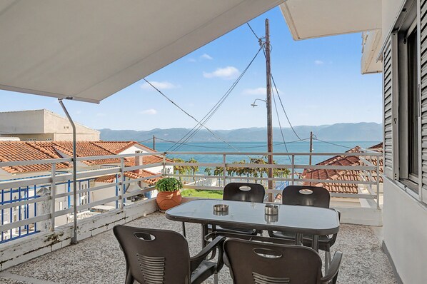 A terrace with a table and chairs, overlooking a body of water and distant mountains.