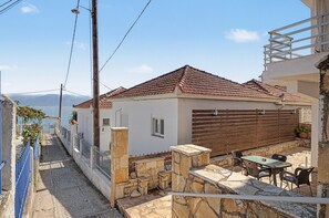 Una propiedad residencial con fachada de piedra, techo de tejas y un pequeño patio con mobiliario exterior.