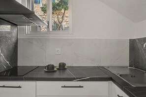 Una cocina con encimera negra, dos teteras, un ventanal y una pared de piedra.