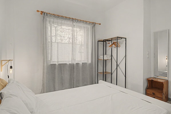 A bedroom with a bed, a wardrobe, a mirror, and a window with curtains.
